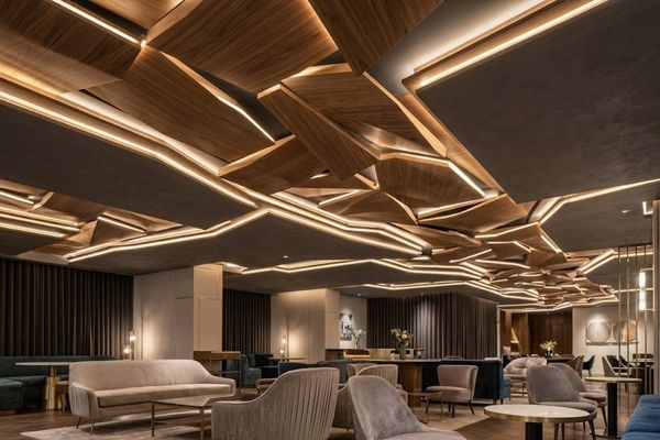 a modern restaurant lounge featuring an innovative custom ceiling design made of sculptural, geometric dark wood panels and integrated linear LED lighting that cast a warm, artistic glow
