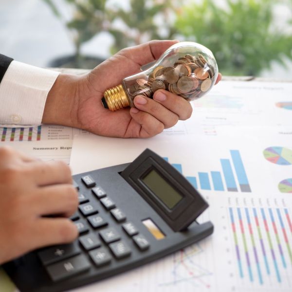 Person holding a lightbulb full of coins in one hand, while typing on a calculator with the other. 