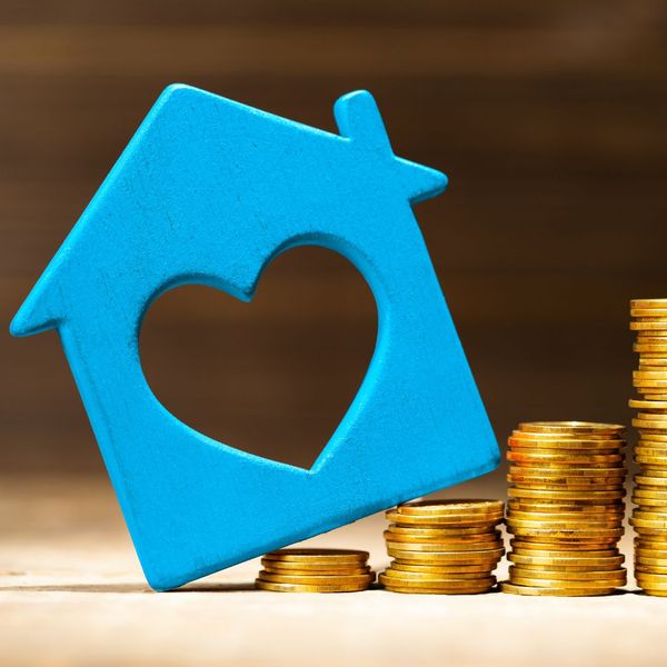 Cutout of a blue house tilted on stacks of coins. 