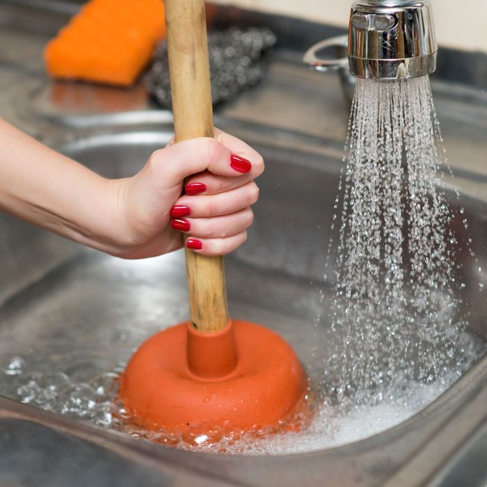 person unclogging sink with plunger