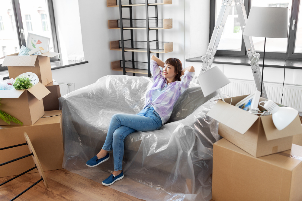 woman sitting on plastic-covered couch, just having moved in to apartment