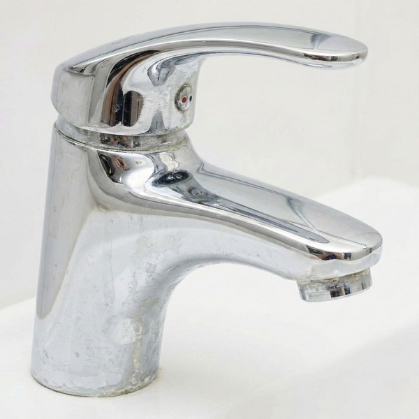 A close-up photograph of a chrome bathroom faucet with visible white limescale and mineral buildup.