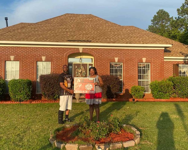 couple holding sign in front of house with new roof