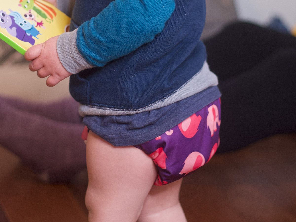 Child with a pacifier holding a book and wearing a diaper from Bum Baby Bum.