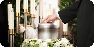 hand on metal urn surrounded with flowers and candles