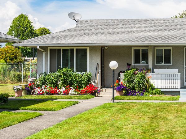 Small residential duplex house with concrete pathway over front yard and blossoming flowers at the entrance