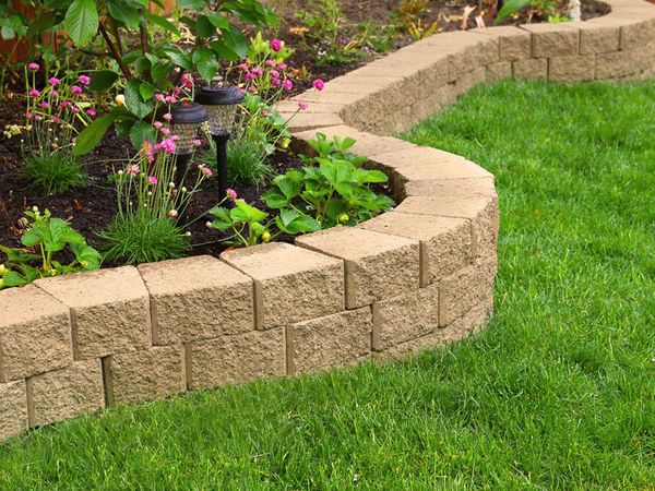 An image of a short stone wall with a garden and beautiful green grass