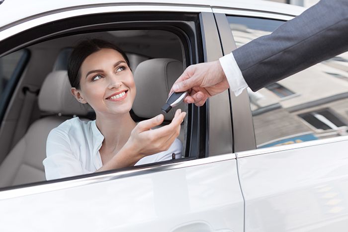 A woman sitting in a car with a man handing her the key