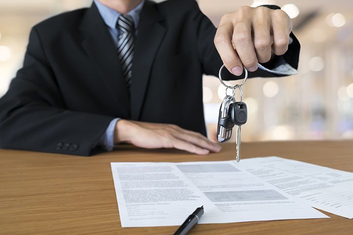  A man in a suit holding a car key over some paperwork