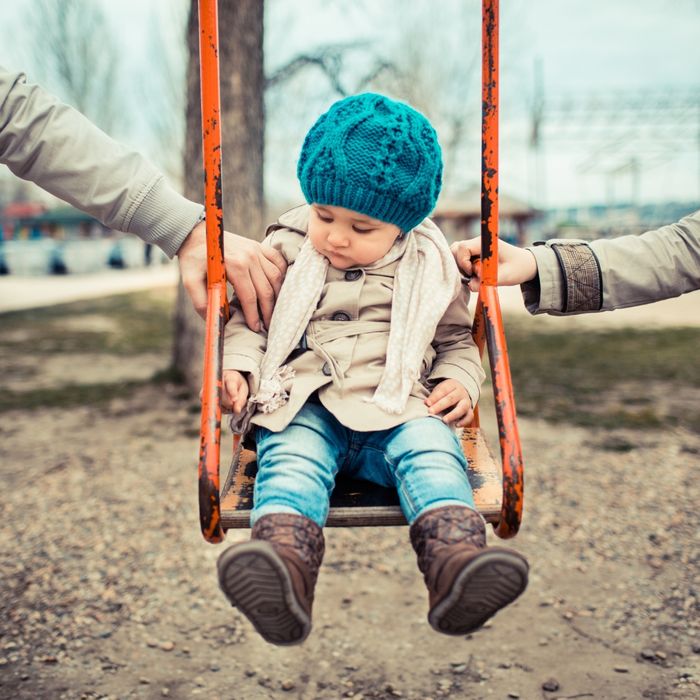 Two hands pushing a child on a swing