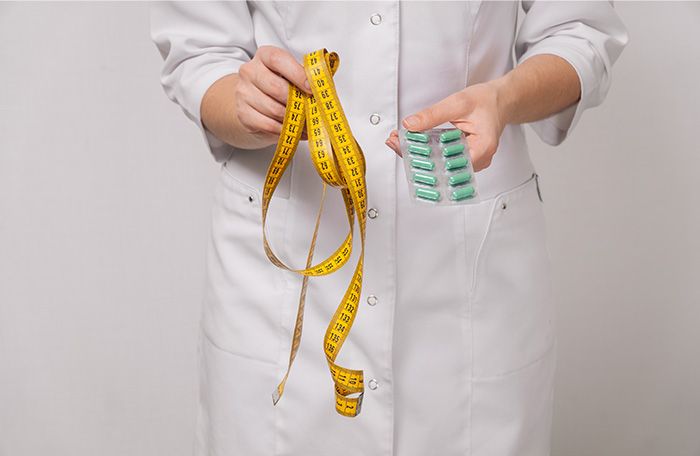 provider holding pills and a measuring tape for weight loss