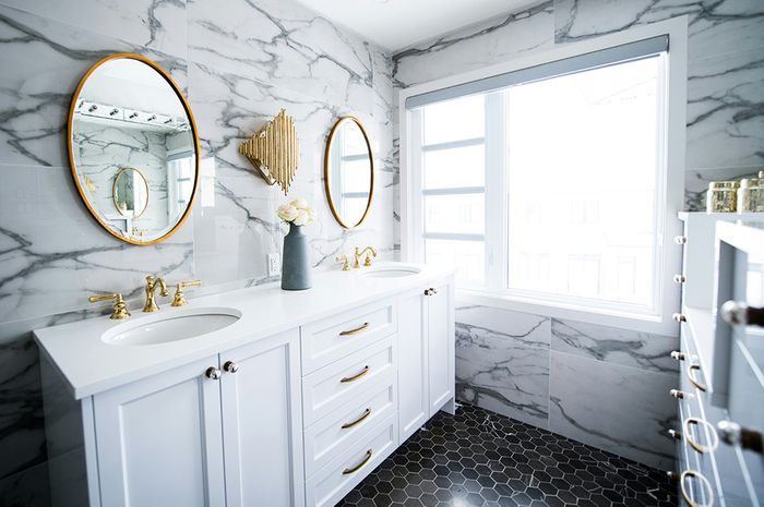 marble bathroom with white cabinets and gold accents