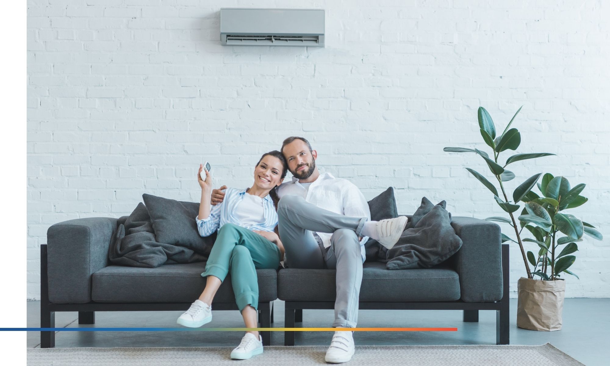 Two people sitting on the couch under a wall mounted AC