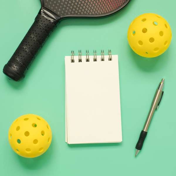 green background with paper, pen and yellow pickleball balls