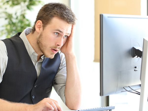 A stressed-looking young man staring at a desktop computer.