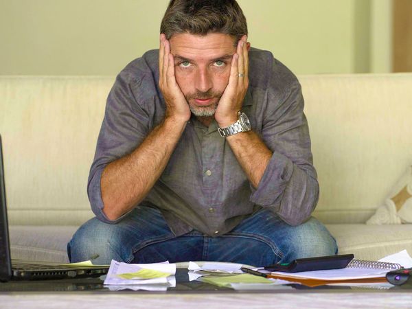 Stressed out man in front of a pile of bills and his computer.