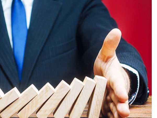 Businessman stopping wooden dominoes from falling with his hand 