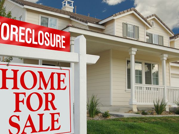  A foreclosure sign on top of a home for sale sign in front of a white house.