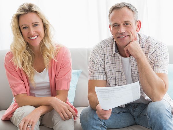 Happy woman and man sitting on a couch with billing statements and a calculator