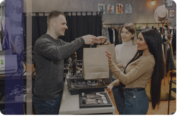 A retail worker handing shopping bags to two women across a counter