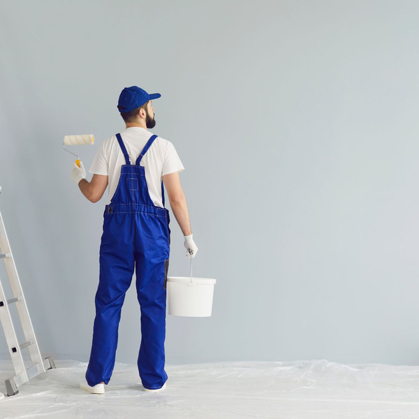Man with paint roller and bucket looking at empty wall