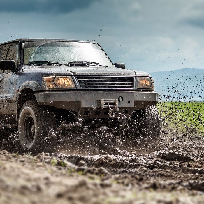 A pickup off-roading on a muddy road with mud flying