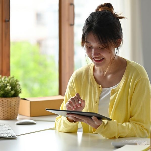woman in yellow cardigan happily using tablet, home office desk