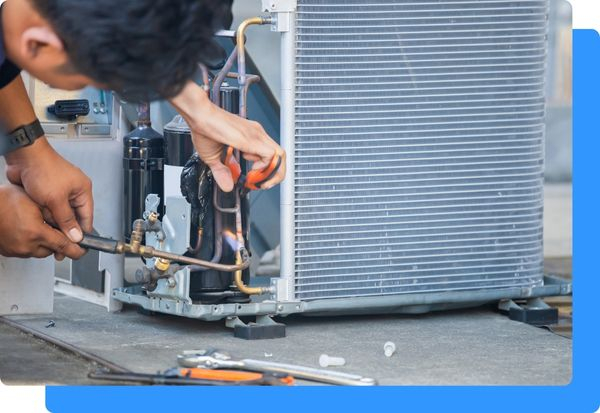 An HVAC tech using a blowtorch on a pipe on an HVAC unit