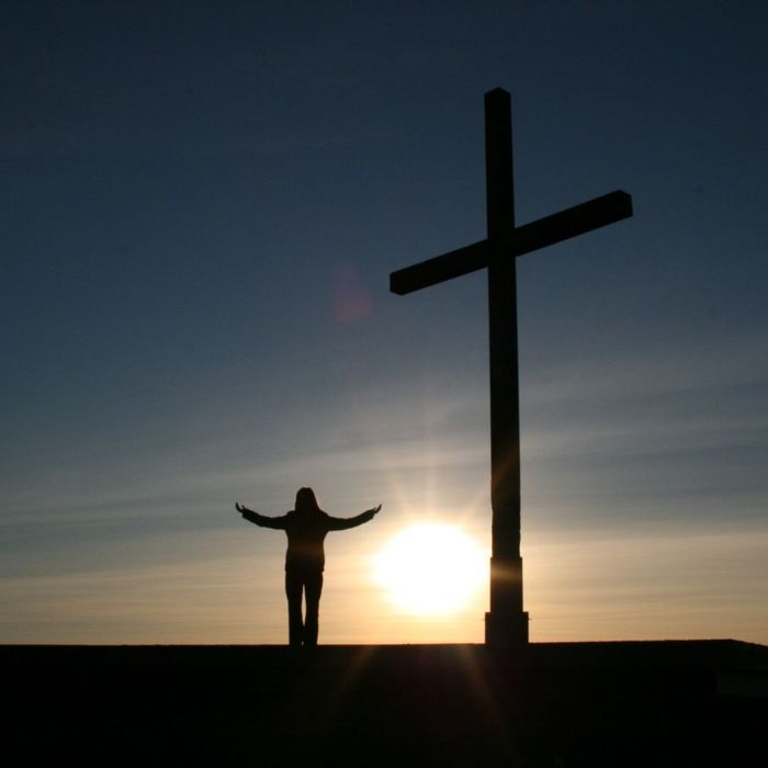 woman standing next to cross at sunrise