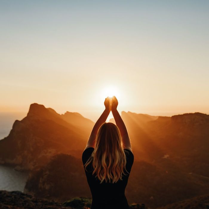 Woman standing in the sunshine holding her arms up. 