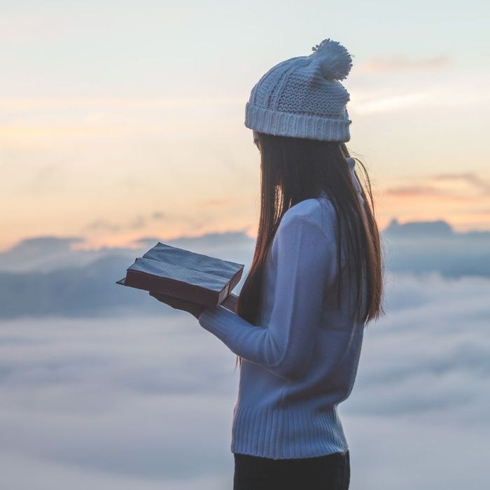 Woman reading a Bible with clouds behind her. 