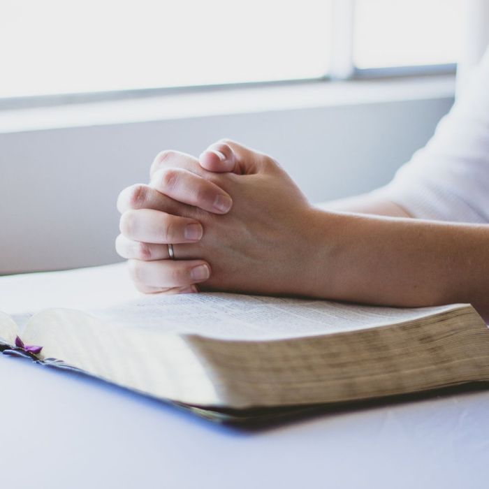 Woman with her hands placed on top of a Bible in prayer. 