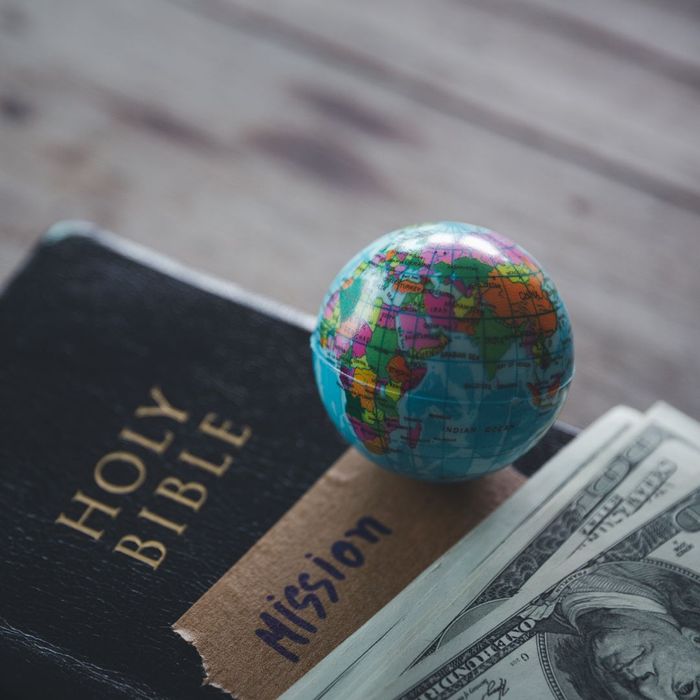 Holy Bible with a piece of cardboard that says "mission," a tiny globe, and cash on it. 