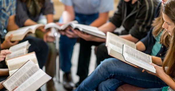 Group of people sitting in a circle reading Bibles. 