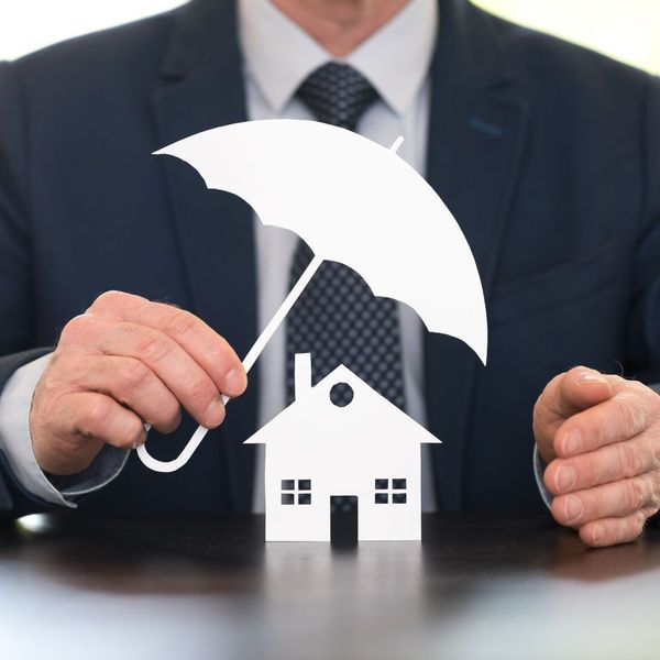 man in a suite holding a small umbrella over a small paper house