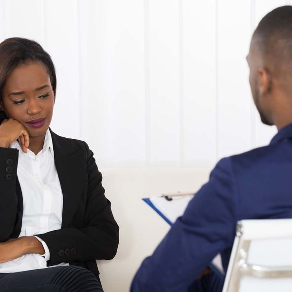 Two people sitting in a room talking, with the woman looking sad. 