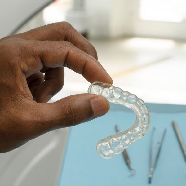 person holding a clear retainer over tools in orthodontist office