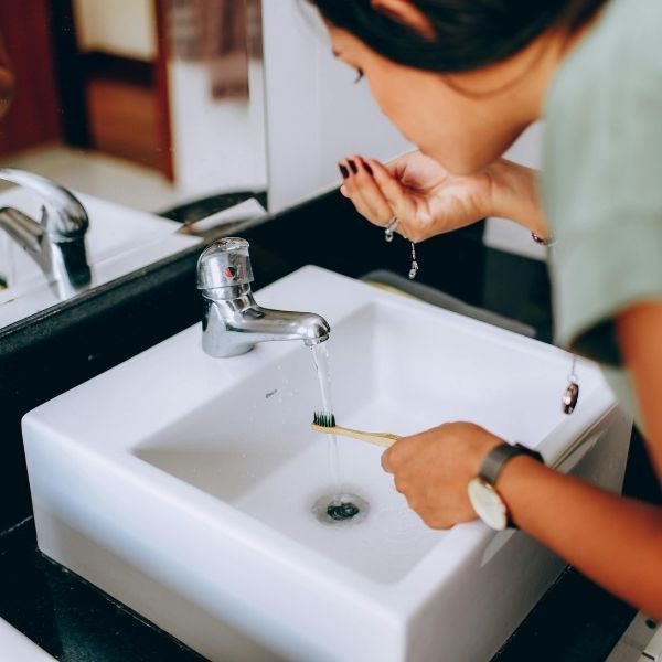 A person rinsing their mouth at a bathroom sink while holding a toothbrush