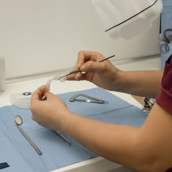 Close-up of a technician's hands carefully repairing a retainer using precision tools