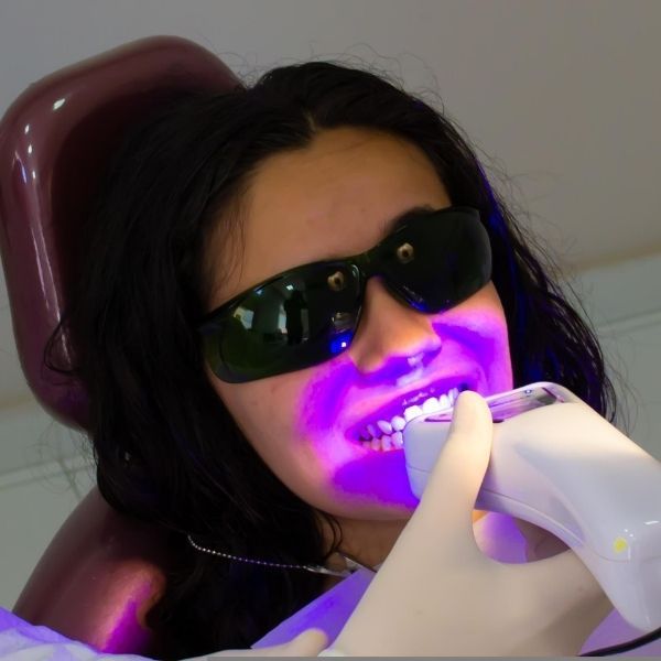 A patient wearing protective eyewear receives professional in-office teeth whitening treatment using an LED light