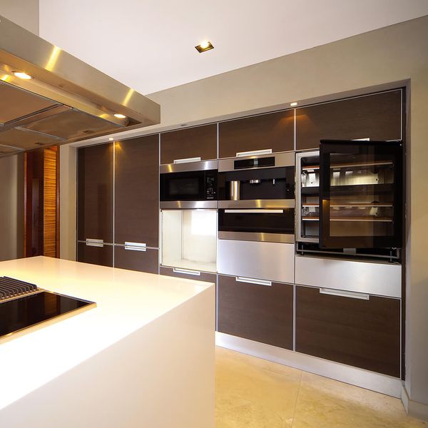 A modern kitchen features a sleek white island with a black cooktop in the foreground. Above the island, a large stainless steel range hood is visible. appliances (1).jpg