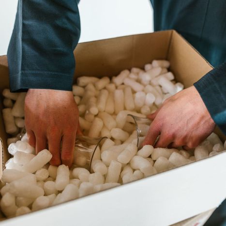 a mover adding glasses to a box of packing peanuts