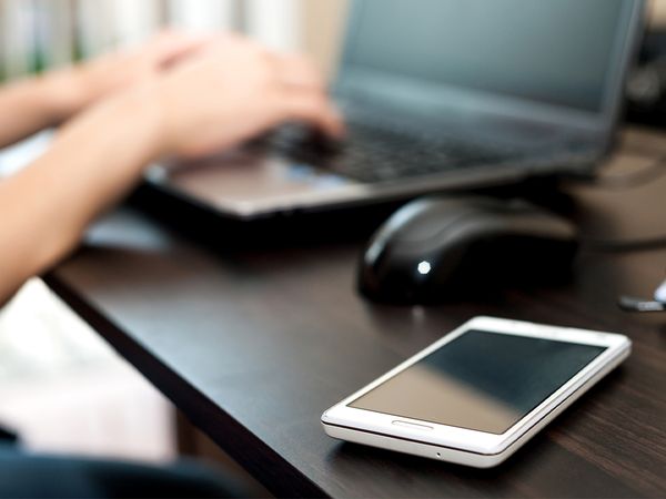 cell phone (smartphone) on a table and woman working on the laptop computer on a background 