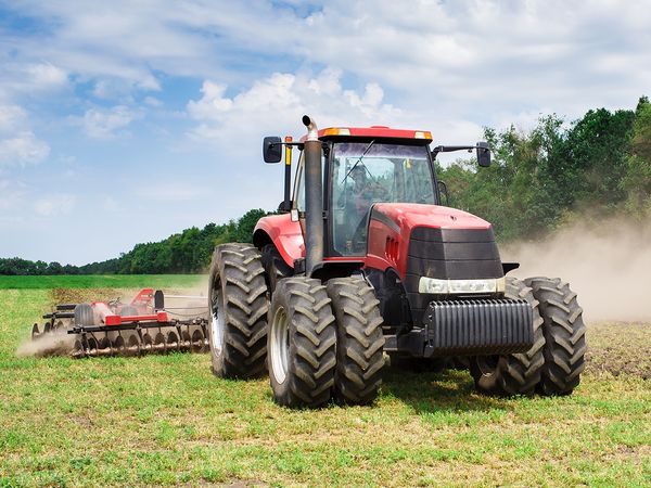 Modern tech red tractor plowing a green agricultural field in spring on the farm