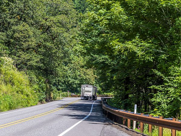 A truck driving down a rural round surrounded by trees.