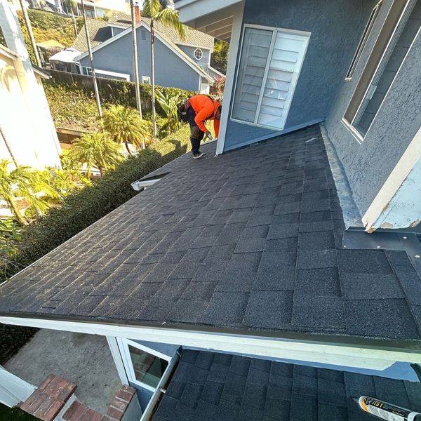 A roofer in safety gear carefully aligns a new architectural shingle on a sunny rooftop.