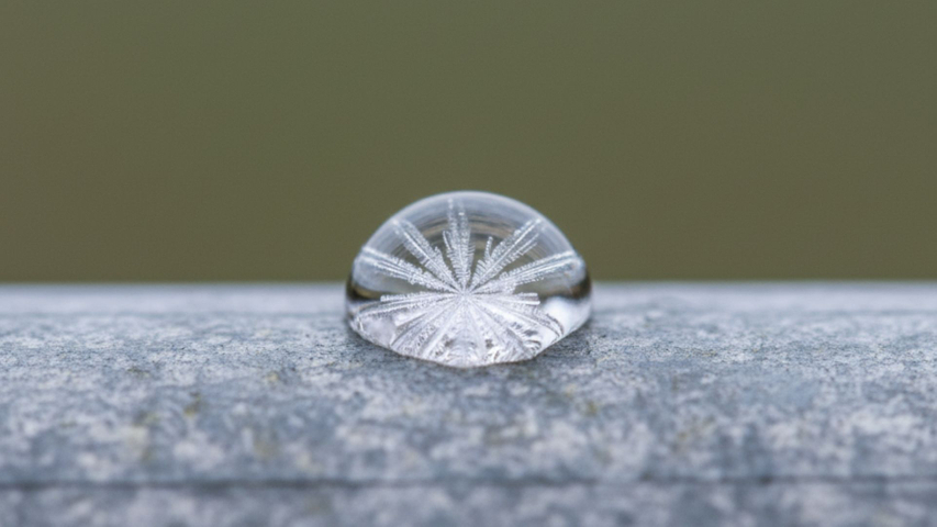 A detailed close-up of a drop of water freezing into ice on a sprinkler system pipe.