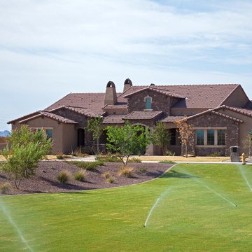 brown house with sprinklers watering the lawn