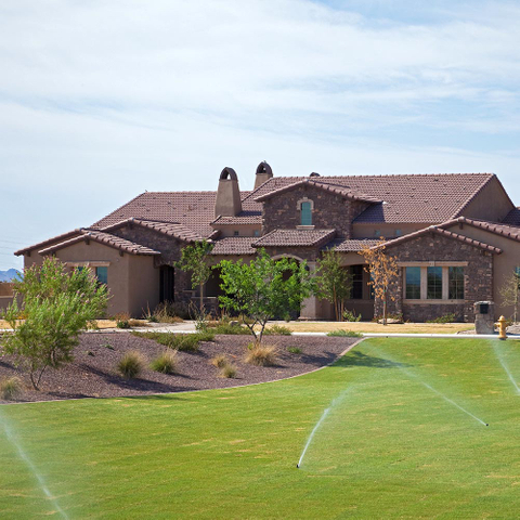 brown house with sprinklers watering the lawn