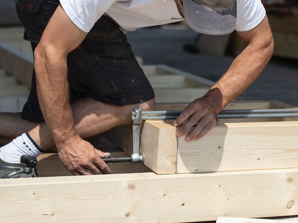 Man putting a metal clamp on a wood structure on a roof